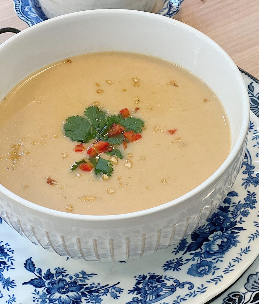 coconut peanut soup in a white bowl with peanut, cilantro and red pepper sprinkled on top.
