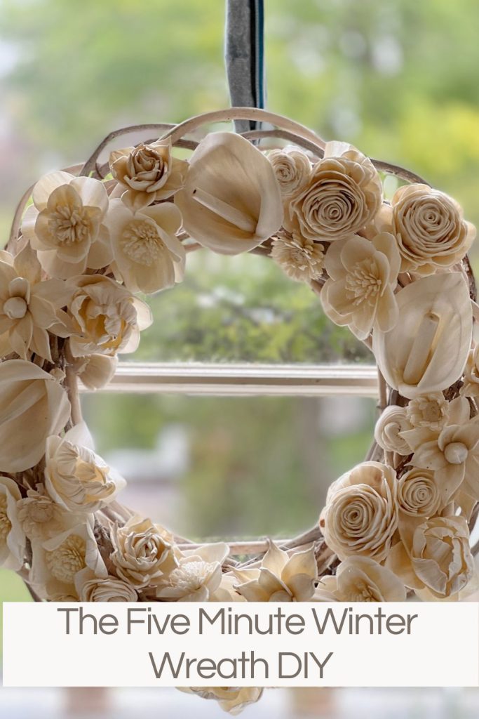 a wreath hanging in a window made with white wood flowers and a grapevine wreath.