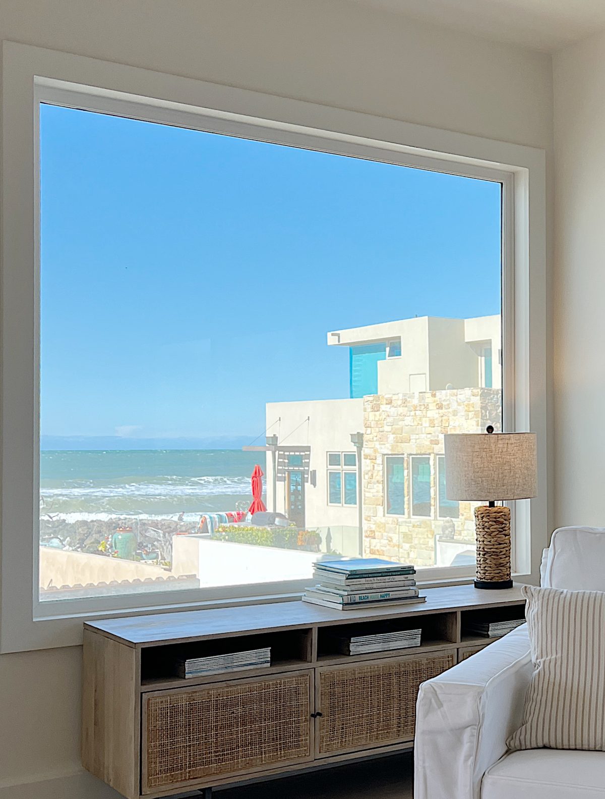 living room of the beach house with a white couch and chair, a fireplace and two light wood tables.