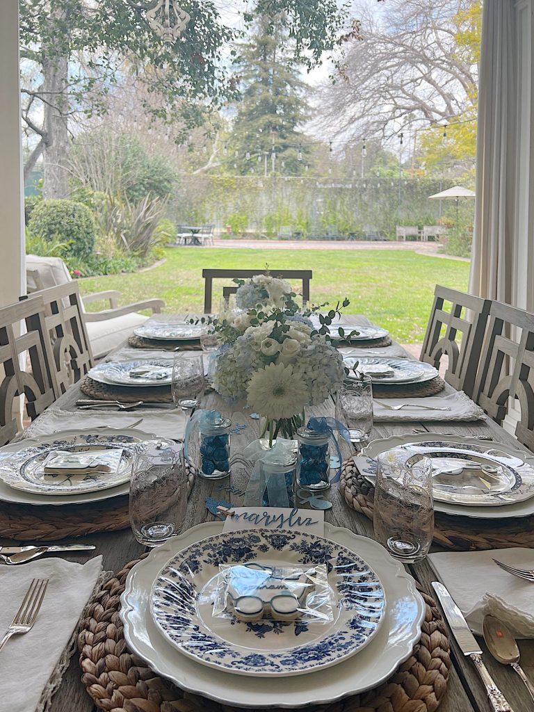 Outdoor table for a baby shower with blue and white plates, flowers, and babythemed decorations.