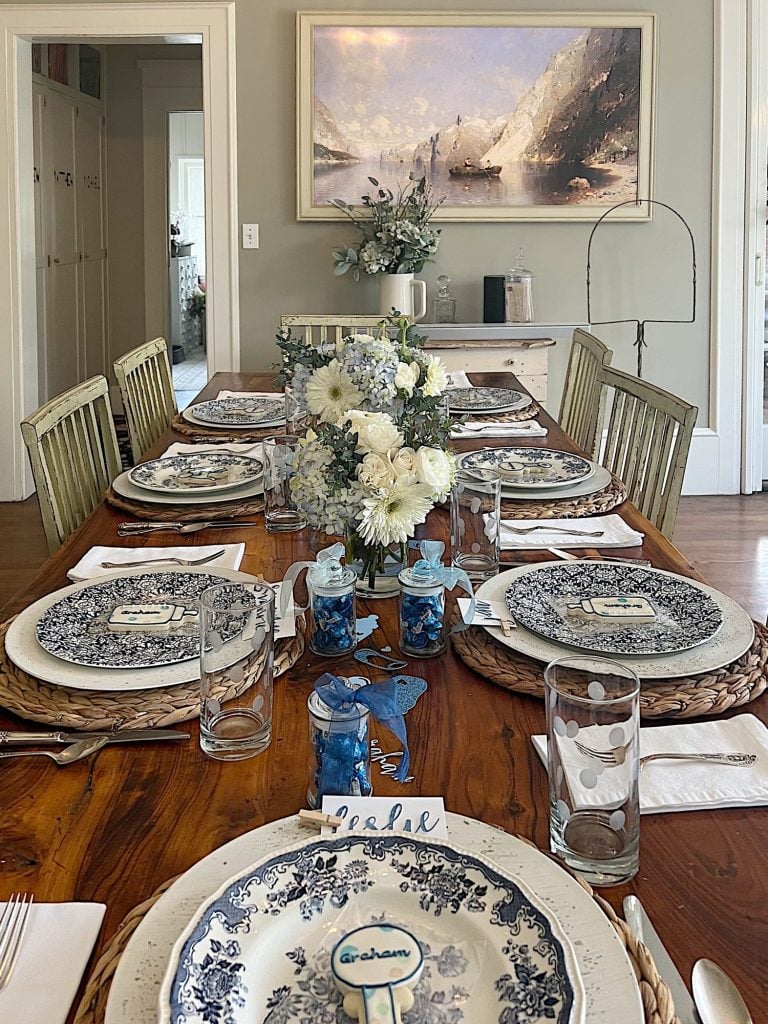 Dining table for a baby shower with blue and white plates, flowers, and babythemed decorations.