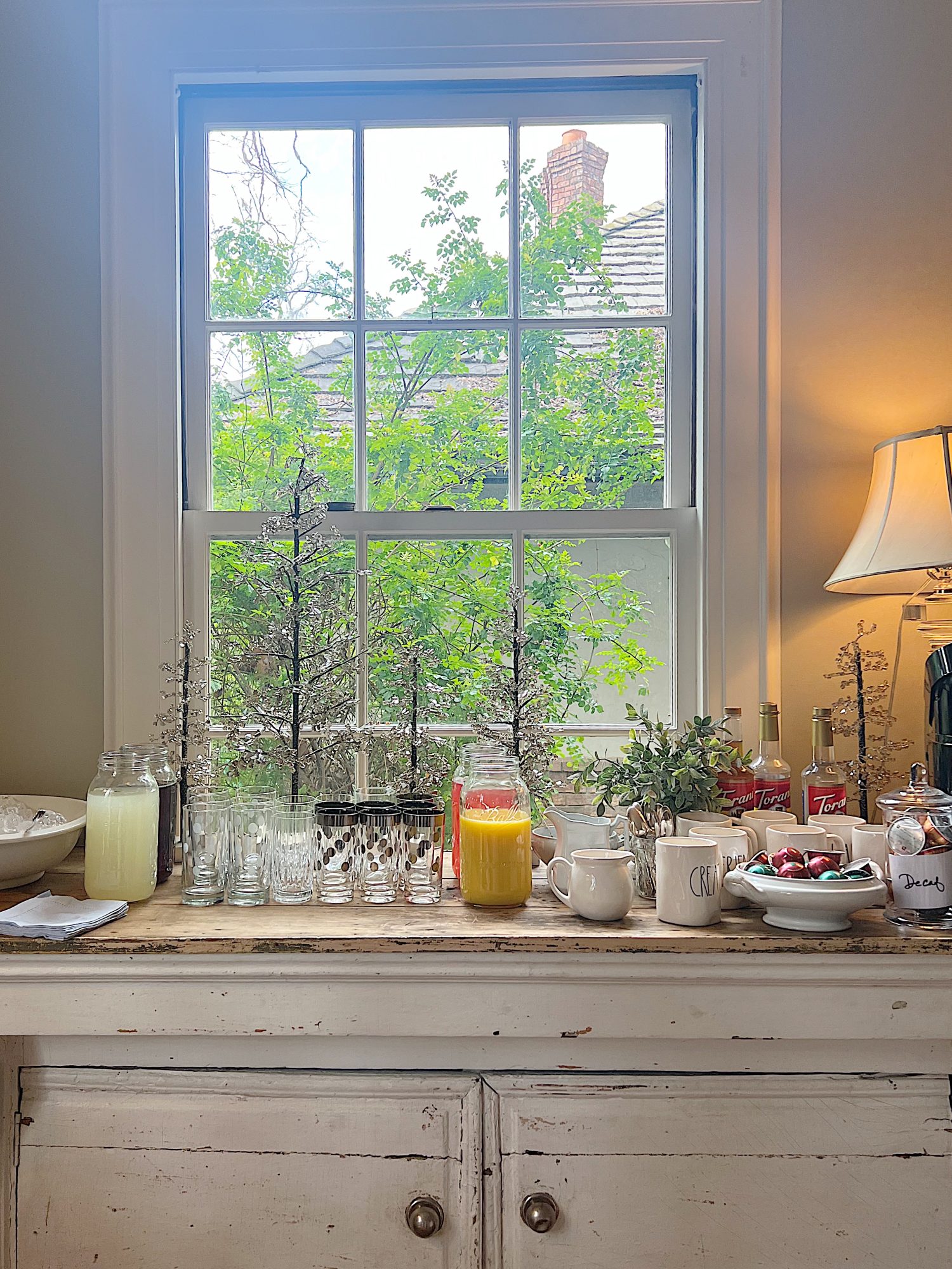Beverage bar for a baby shower with coffee maker and flavored syrups, juices, glasses, and ice.