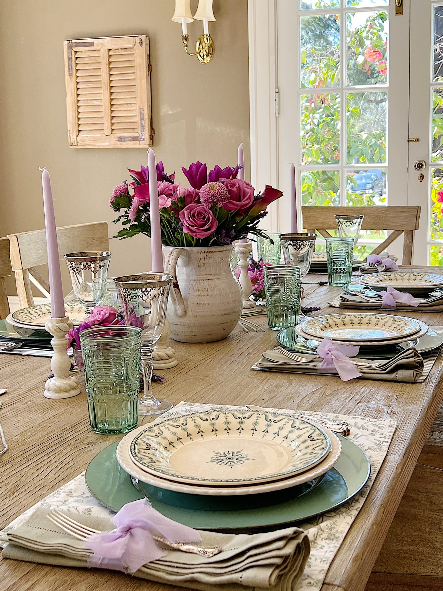 A spring table set in the dining room with green and white plates and napkins, lavender ties, green and sil