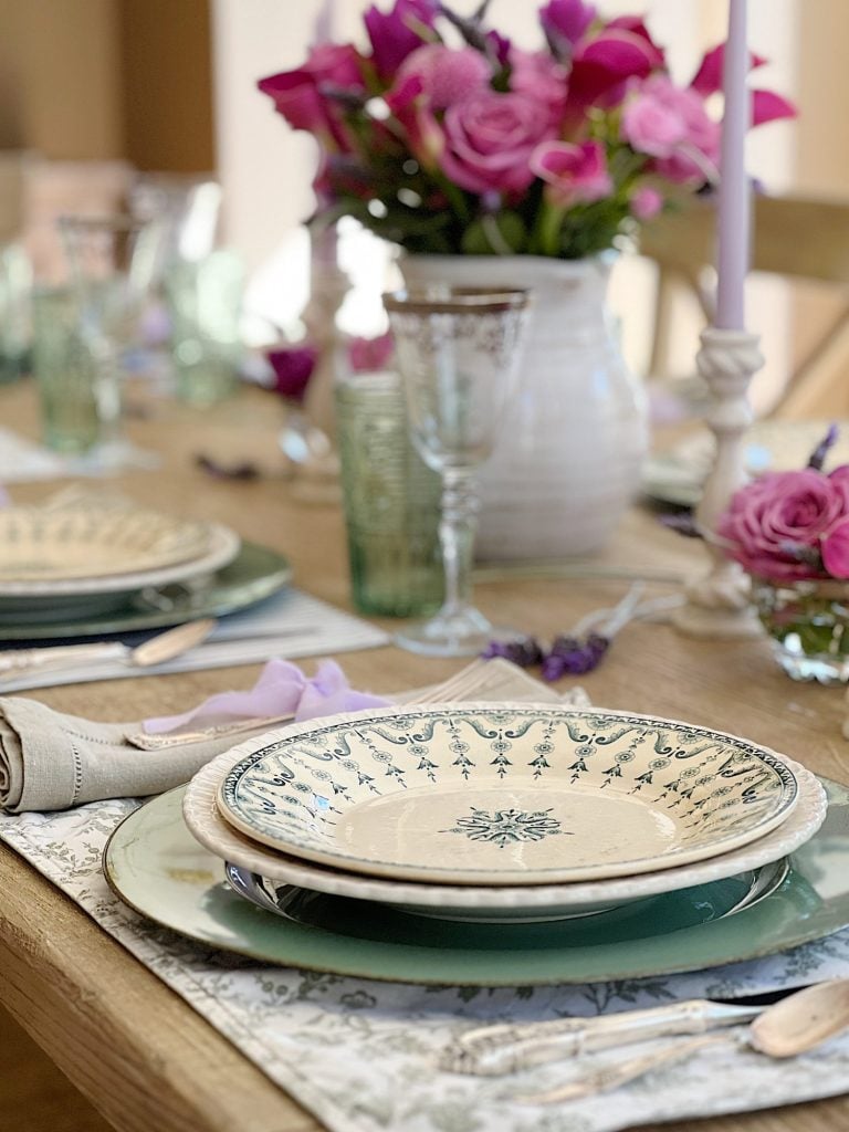 A spring table set in the dining room with green and white plates and napkins, lavender ties, green and sil