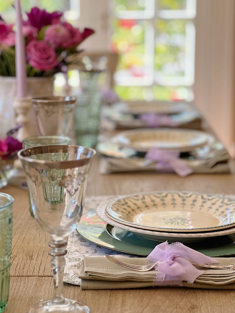 A spring table set in the dining room with green and white plates and napkins, lavender ties, green and sil