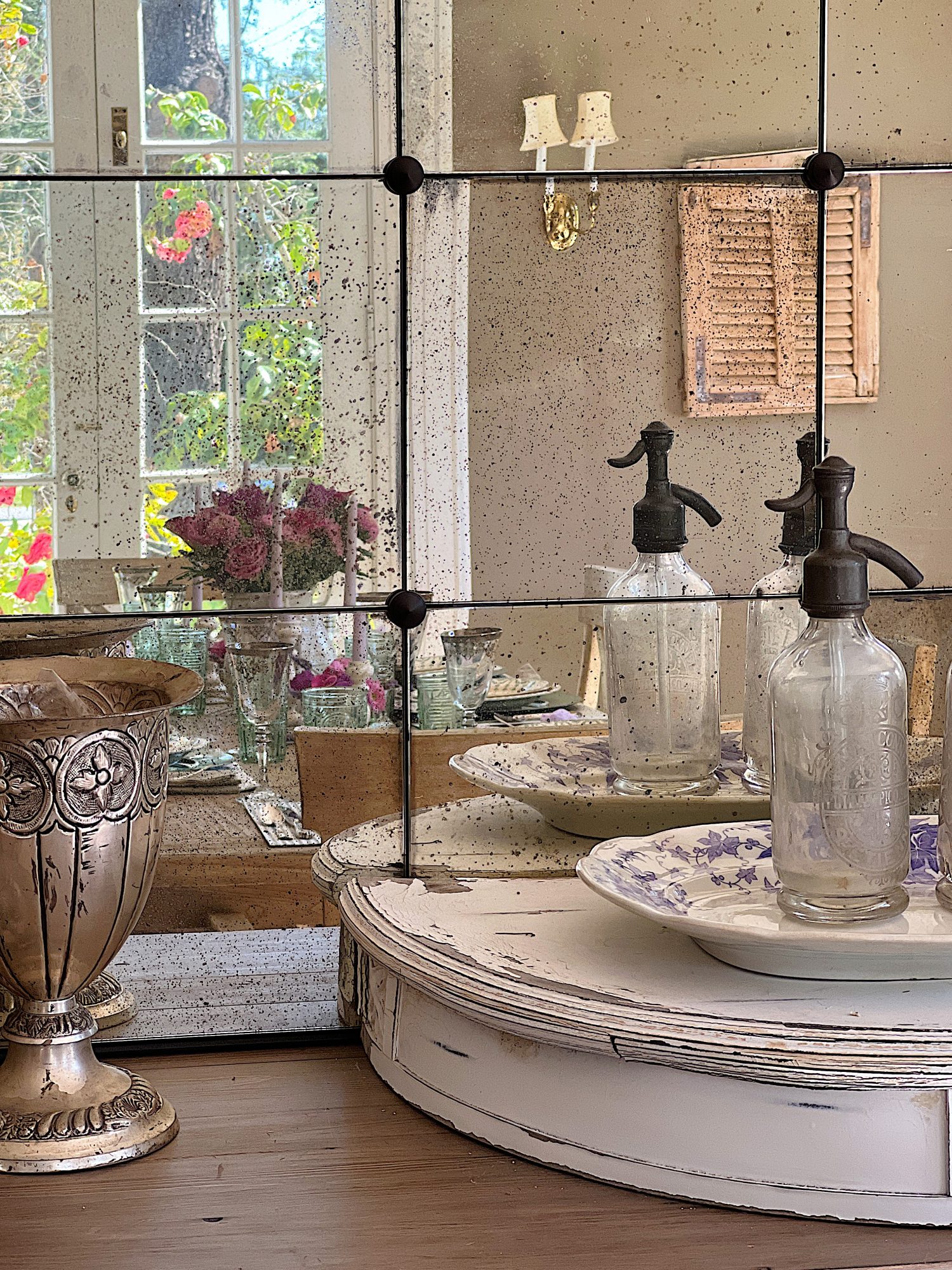 Reflection in the mirror of a spring table set in the dining room with green and white plates and napkins, lavender ties, green and sil