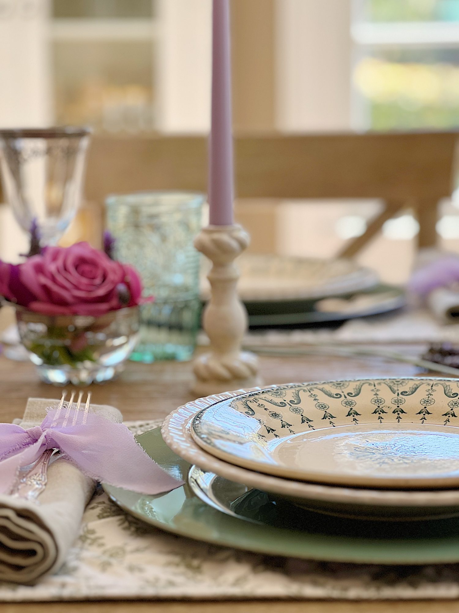 A spring table set in the dining room with green and white plates and napkins, lavender ties, green and sil