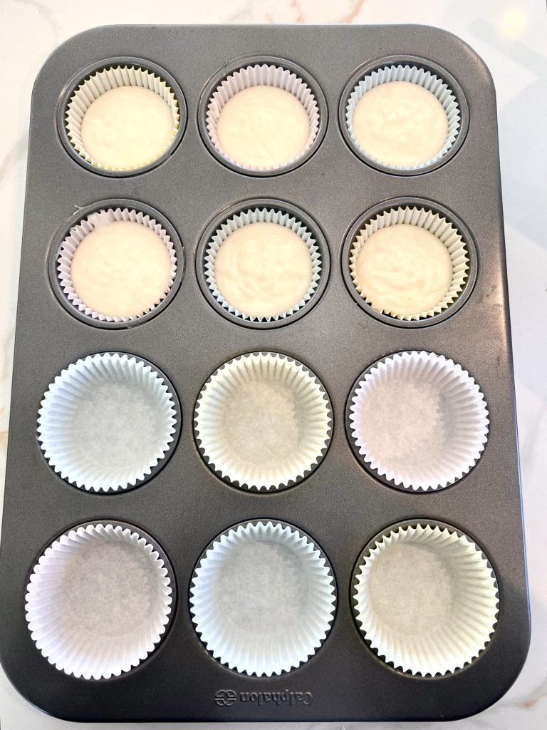 Muffin/Cupcake tin with pastel liners. Half of the liners are filled with cupcake batter