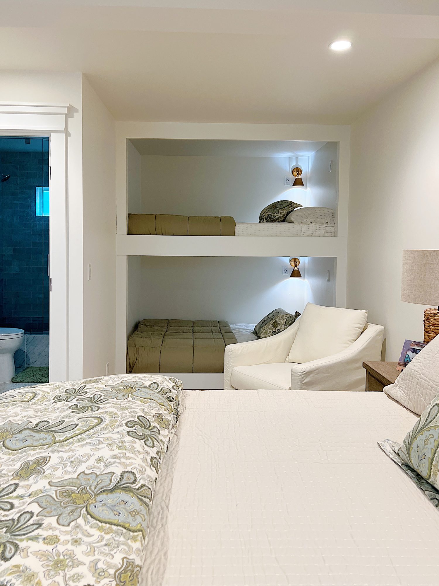 A bedroom with two built in queen sized bunk beds, a king sized bed, rocking chair and green, tan, and blue decor.
