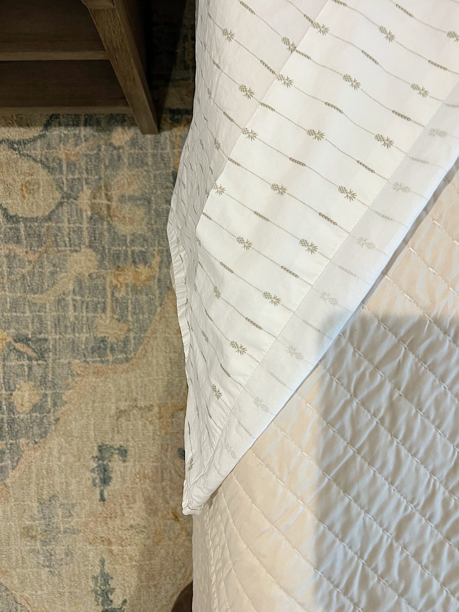 Close up of green and white pineapple decorated sheets from Tommy Bahama and a blue and tan rug from Alexander home.