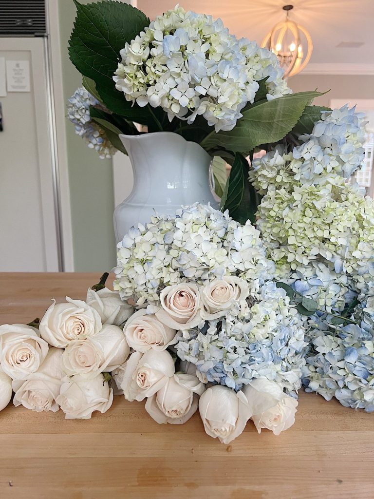 white roses and light blue hydrangeas and a white vase on a counter.