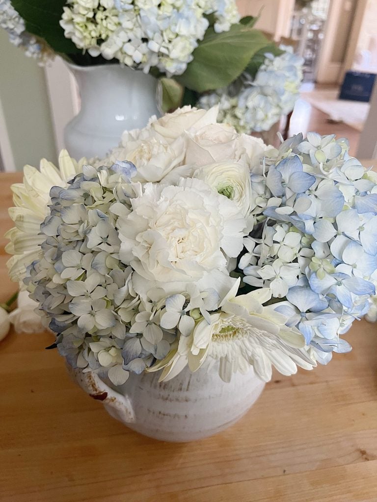 Two white vases filled with white and light blue flowers.