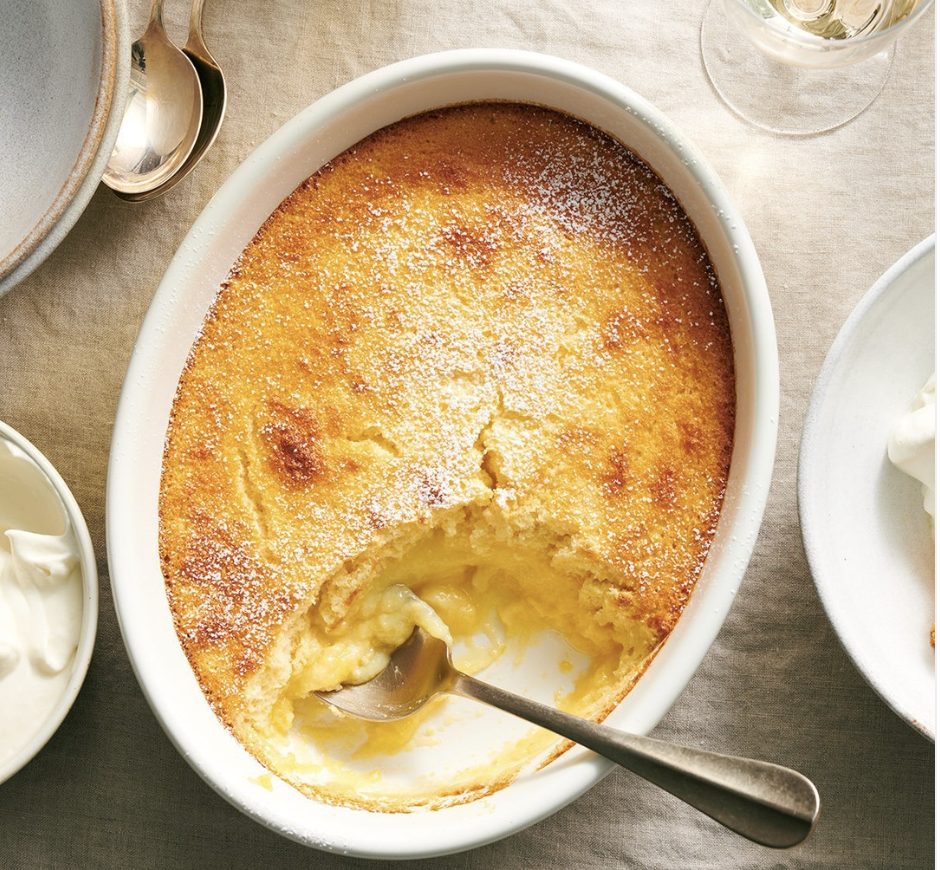 Oval white dish with a silver spoon and baked lemon pudding. There is a large portion gone from the dish and the inside looks like s creamy souffle