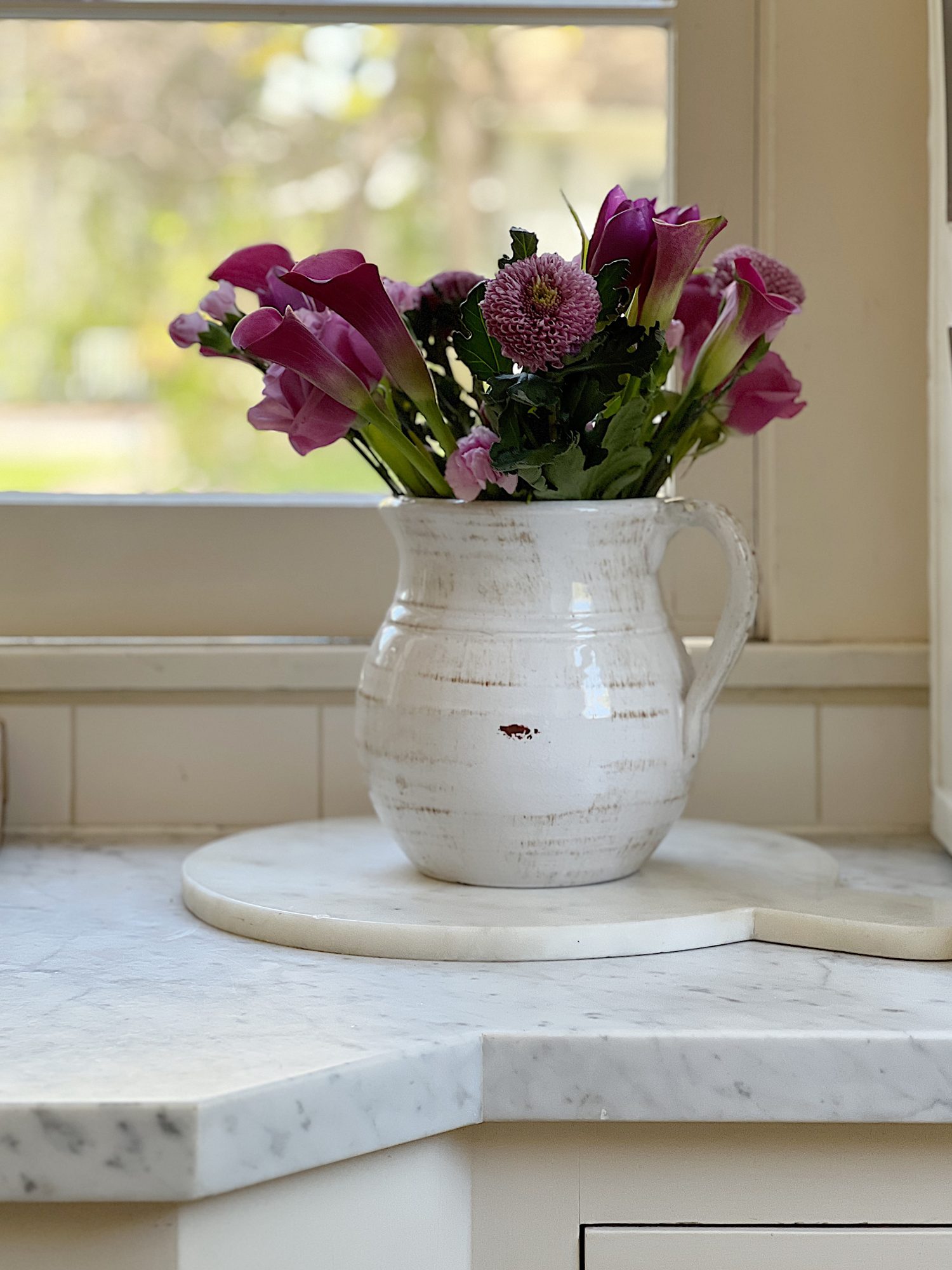 A traditional kitchen with white cabinets and light green walls and white marble countertops decorated with sage green and lavender items for spring.