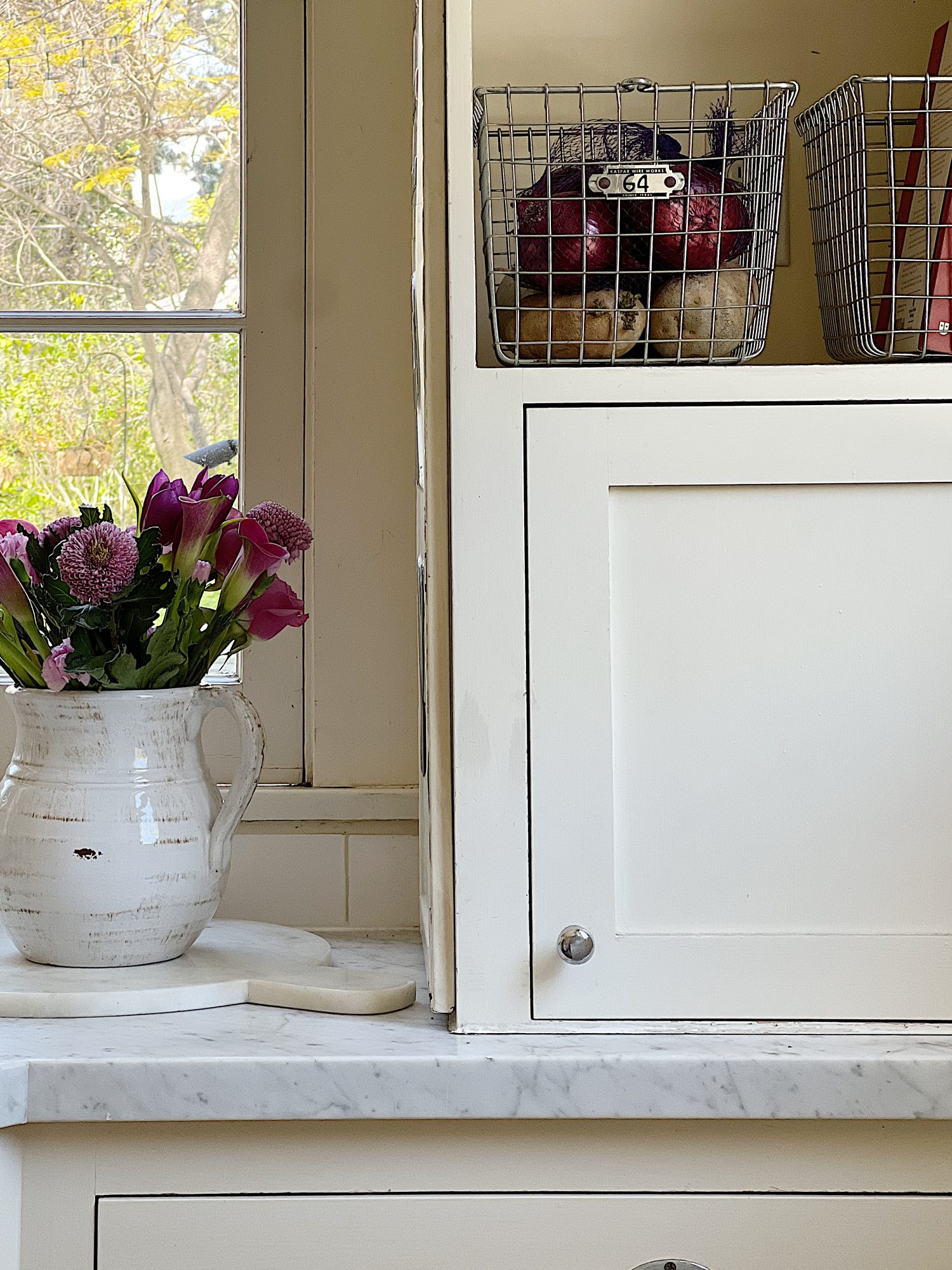 A traditional kitchen with white cabinets and light green walls and white marble countertops decorated with sage green and lavender items for spring.