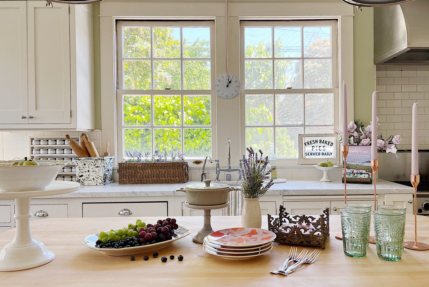 A traditional kitchen with white cabinets and light green walls and a butcher block kitchen island decorated with sage green and lavender items for spring.