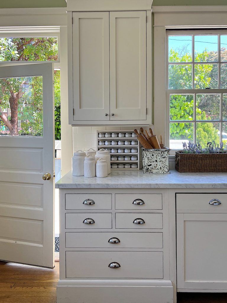 A traditional kitchen with white cabinets and light green walls and a butcher block kitchen island decorated with sage green and lavender items for spring.
