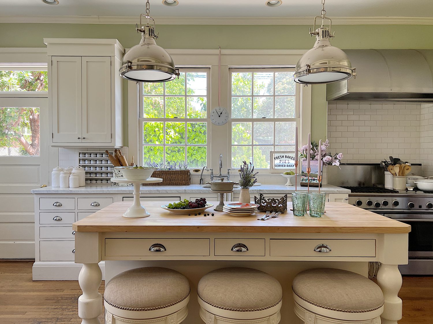 A traditional kitchen with white cabinets and light green walls and a butcher block kitchen island decorated with sage green and lavender items for spring.