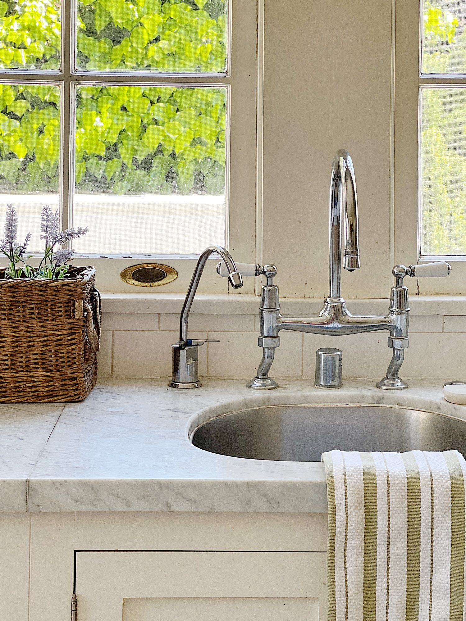 A traditional kitchen with white cabinets and light green walls and white marble countertops decorated with sage green and lavender items for spring.