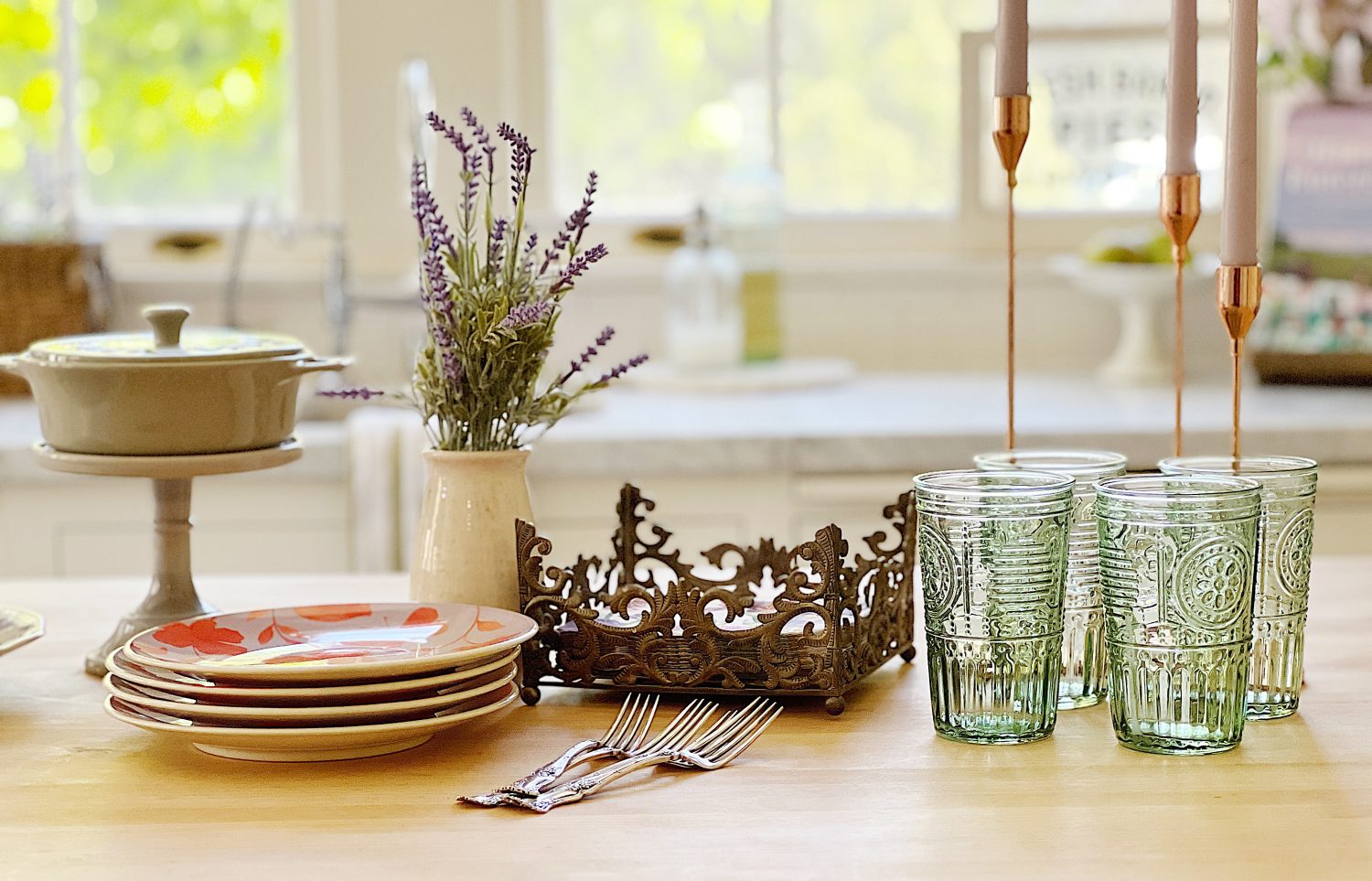 A traditional kitchen with white cabinets and light green walls and a butcher block kitchen island decorated with sage green and lavender items for spring.