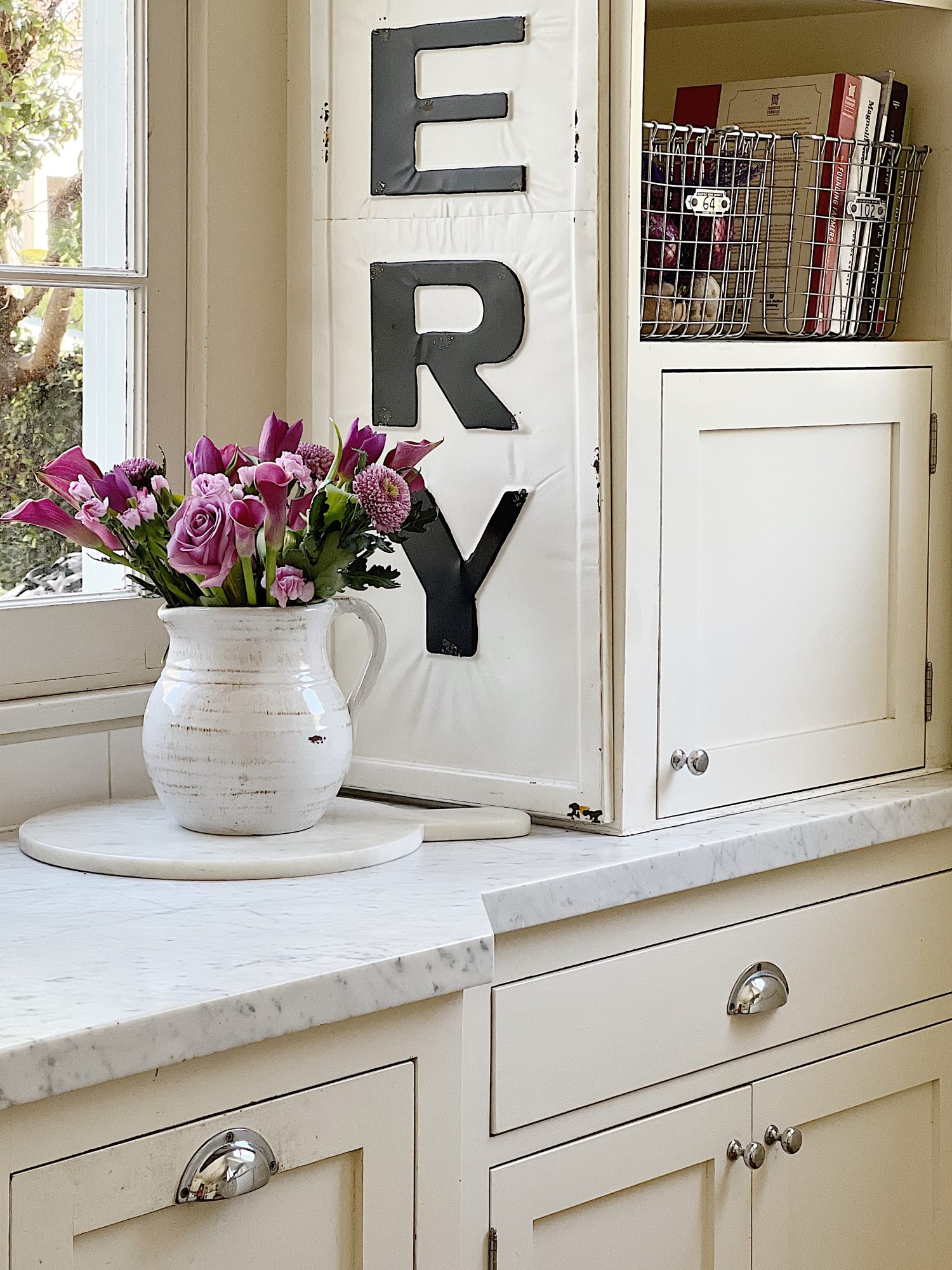 A traditional kitchen with white cabinets and light green walls and white marble countertops decorated with sage green and lavender items for spring.