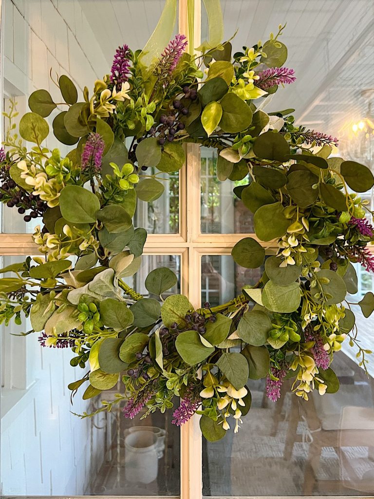 a eucalyptus wreath with lavender and white flowers hanging on a door.