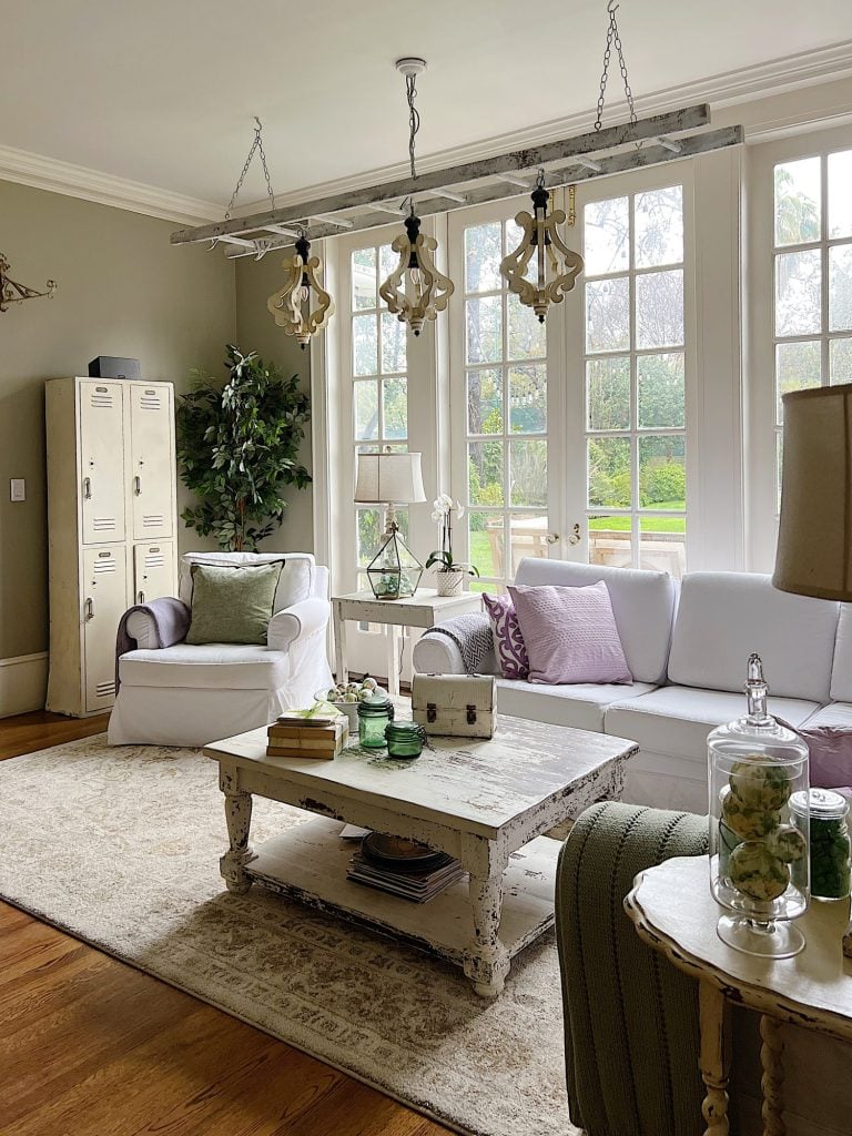 New spring home decor in the family room with lavender throws and pillows and sage green jars, a wreath and small decor items.
