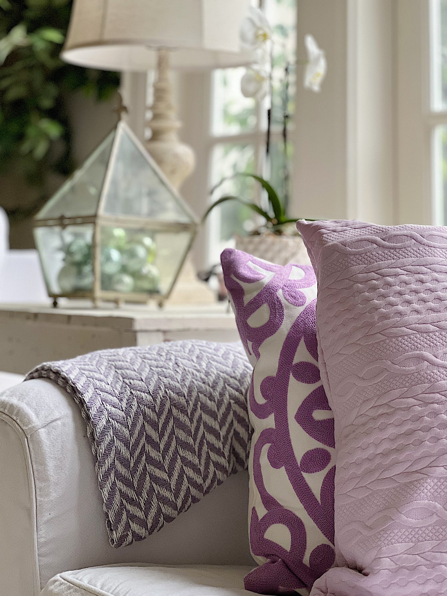 New spring home decor in the family room with lavender throws and pillows and sage green jars, a wreath and small decor items.
