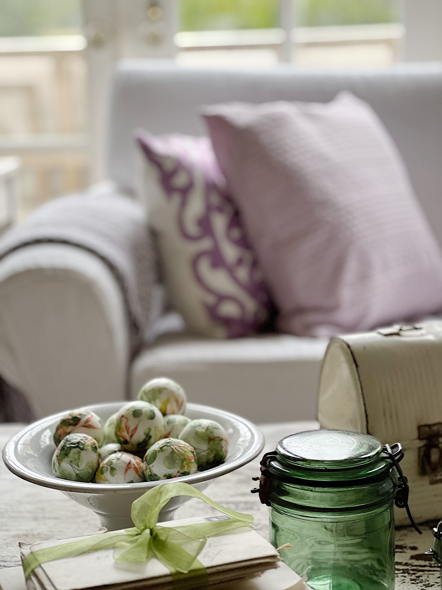 New spring home decor in the family room with lavender throws and pillows and sage green jars, a wreath and small decor items.