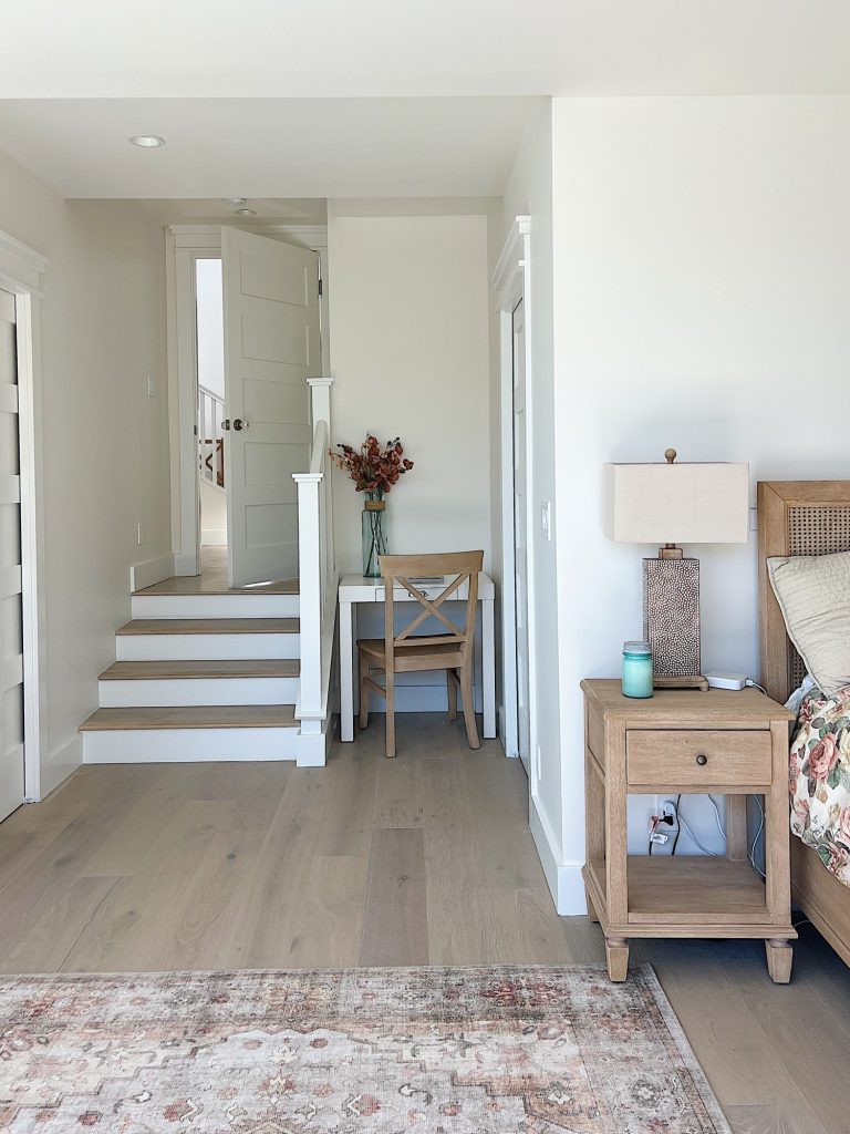 Primary bedroom entrance with small staircase, light wood bed, floral rug and small white desk with chair.