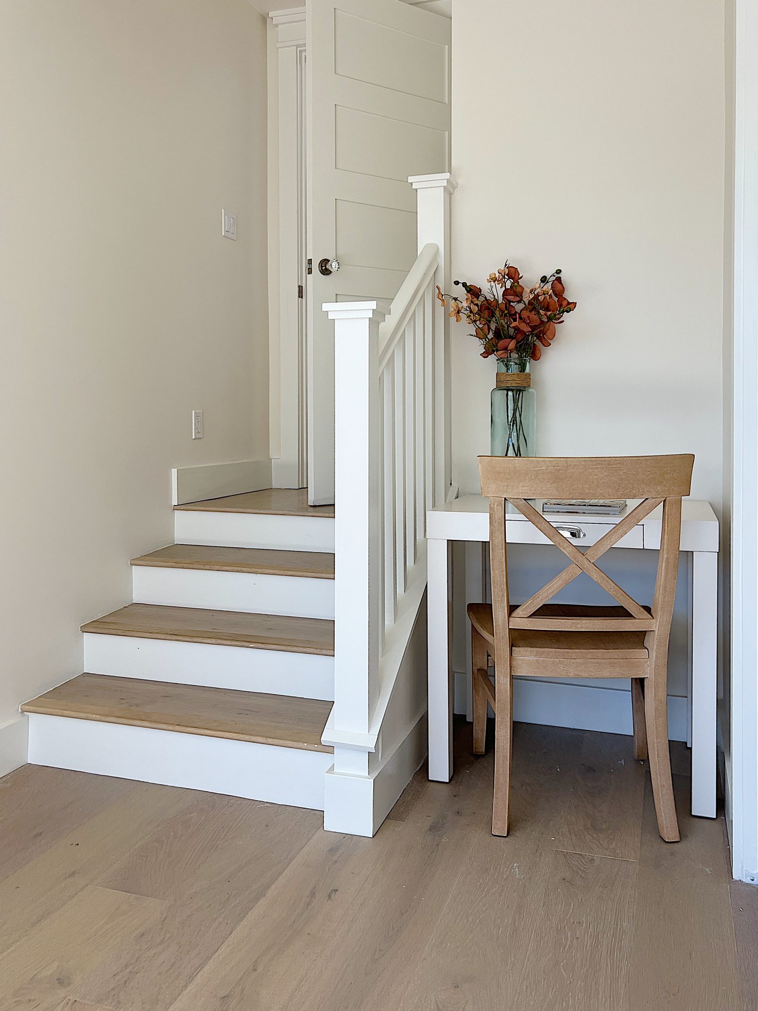 Primary bedroom entrance with small staircase, light wood bed, floral rug and small white desk with chair.
