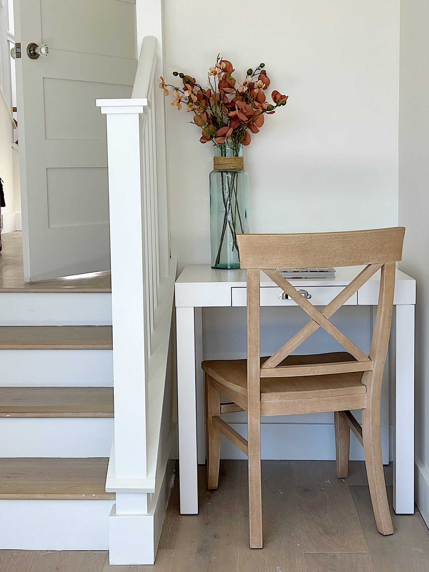 Primary bedroom entrance with small staircase, light wood bed, floral rug and small white desk with chair.
