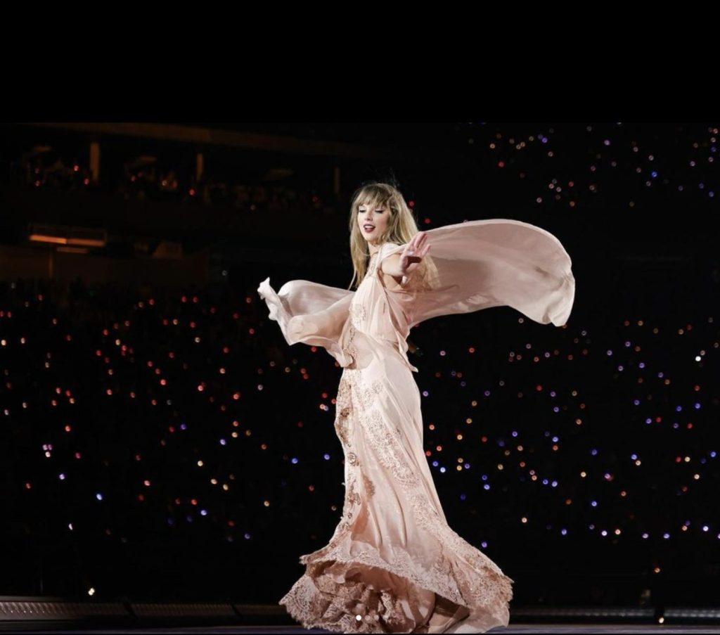 Taylor Swift onstage in a flowy irredescent pink gown during her Eras Tour concert 