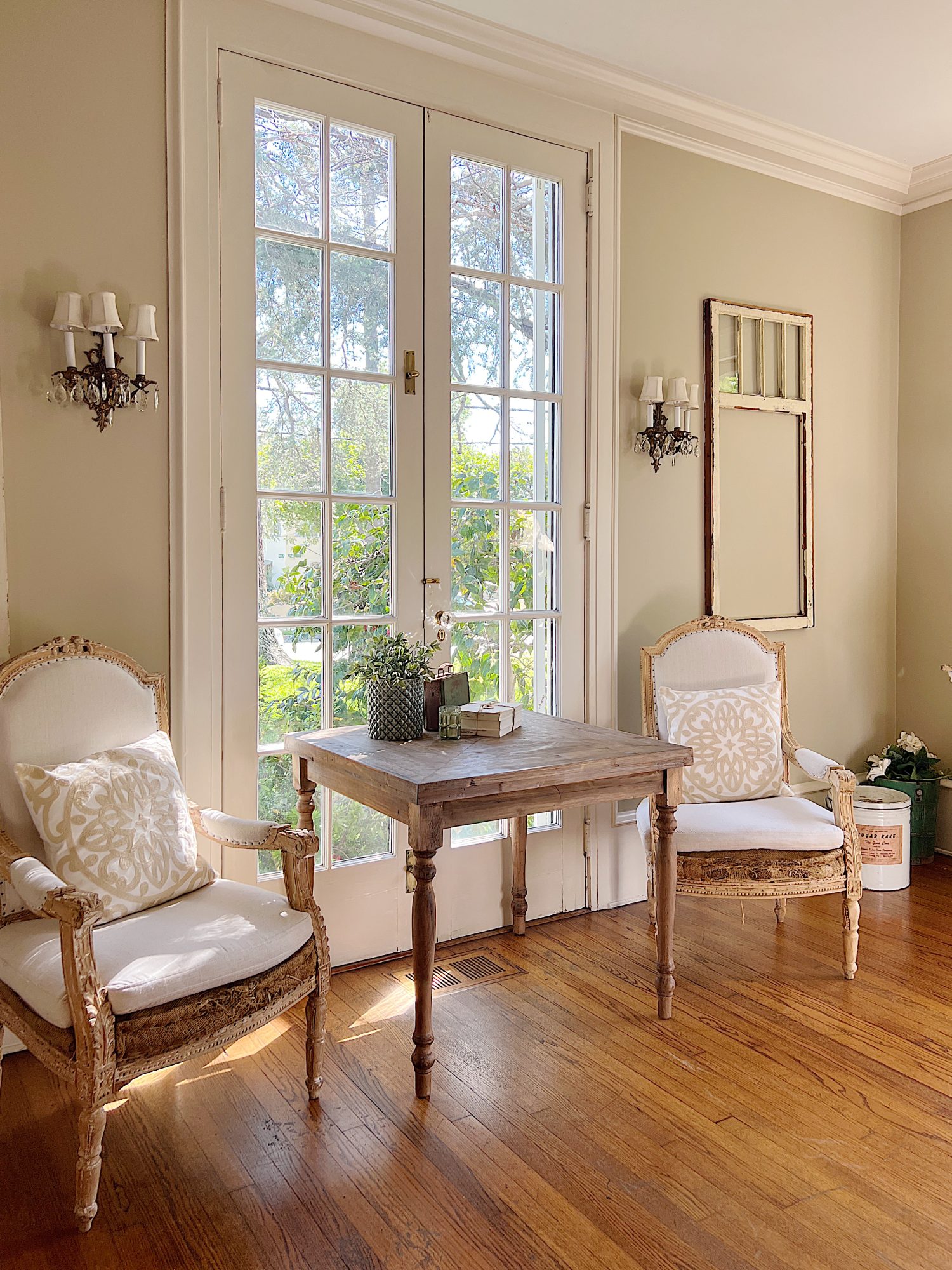 A large living room with two white couches, a landscape painting above the mantle, sage green and lavender pillows, lavender throws, and spring decor.