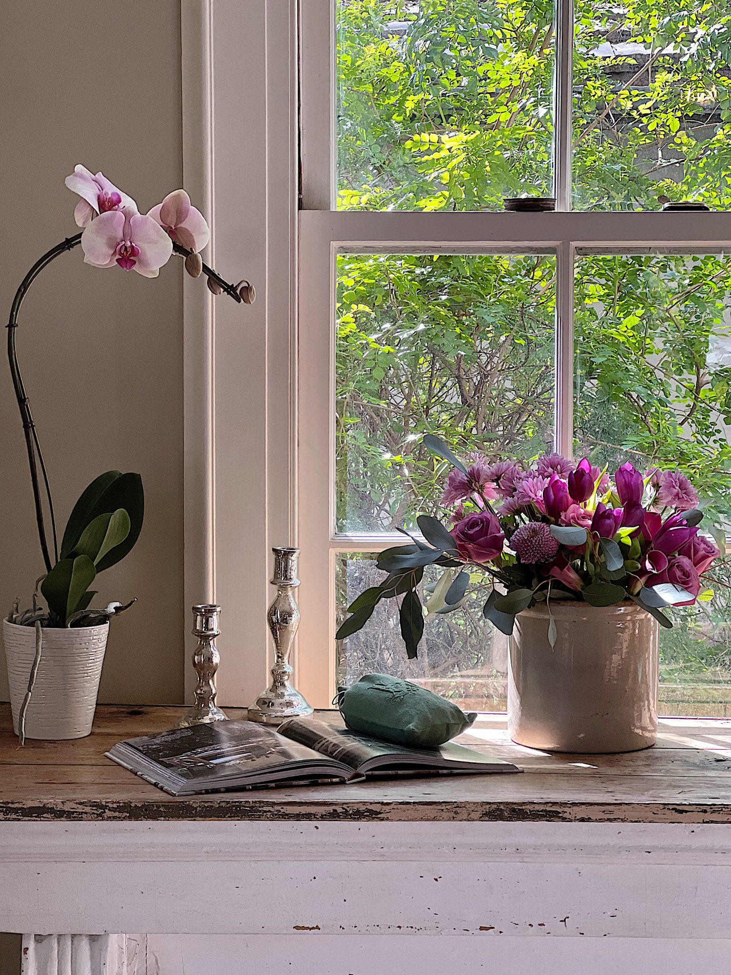 A large living room with two white couches, a landscape painting above the mantle, sage green and lavender pillows, lavender throws, and spring decor.