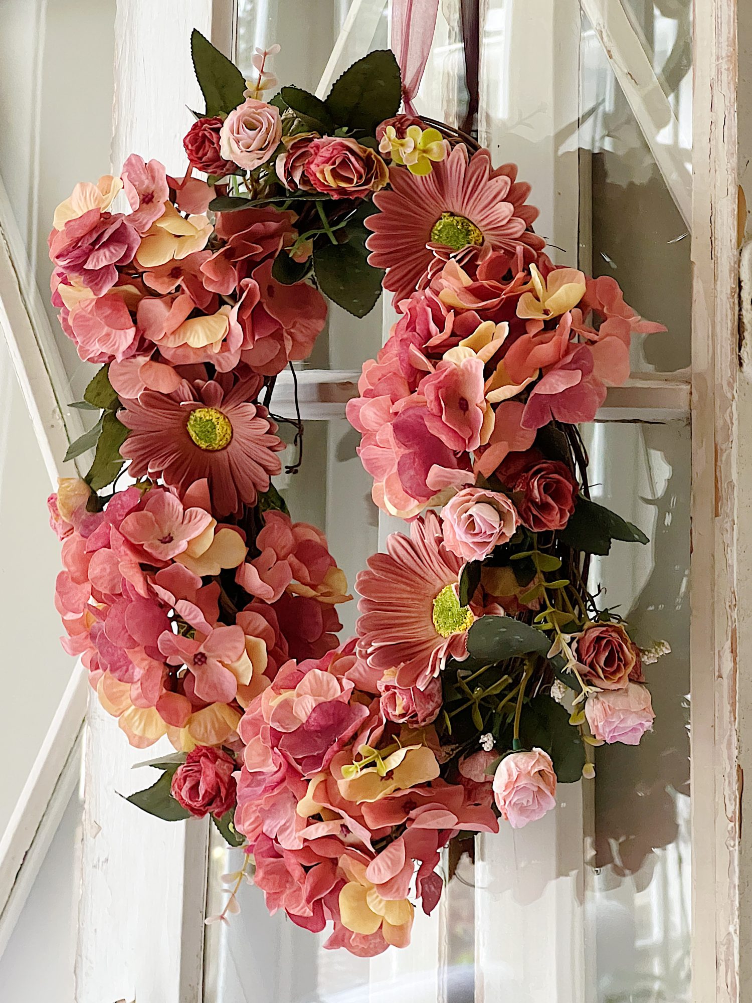 Handmade wreath consisting of faux hydrangeas, gerbera daisies, and roses attached to a grapevine wreath