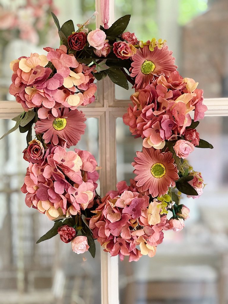 Handmade wreath consisting of faux hydrangeas, gerbera daisies, and roses attached to a grapevine wreath