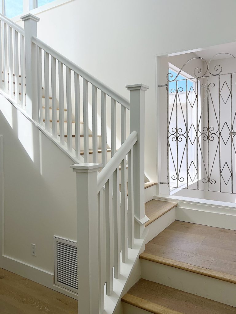 A metal gate painted white and gold installed in an opening on a staircase remodel.