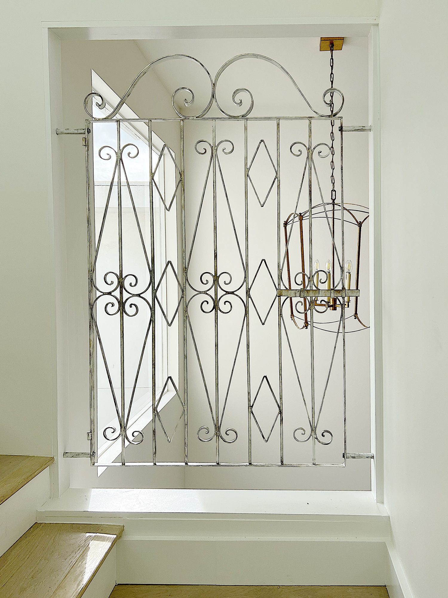 A metal gate painted white and gold installed in an opening on a staircase remodel.