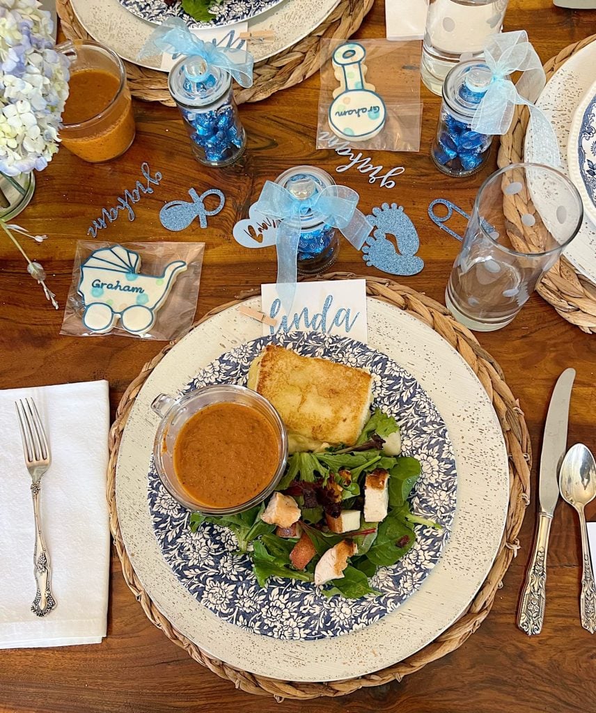 A blue and white plate with soup, a grilled cheese sandwich, and salad on a decorated table.