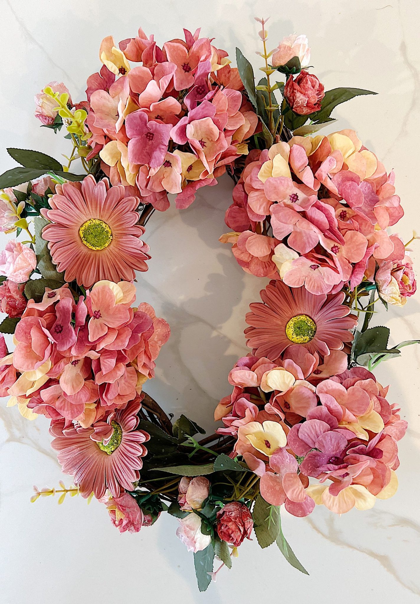 Handmade wreath consisting of faux hydrangeas, gerbera daisies, and roses attached to a grapevine wreath