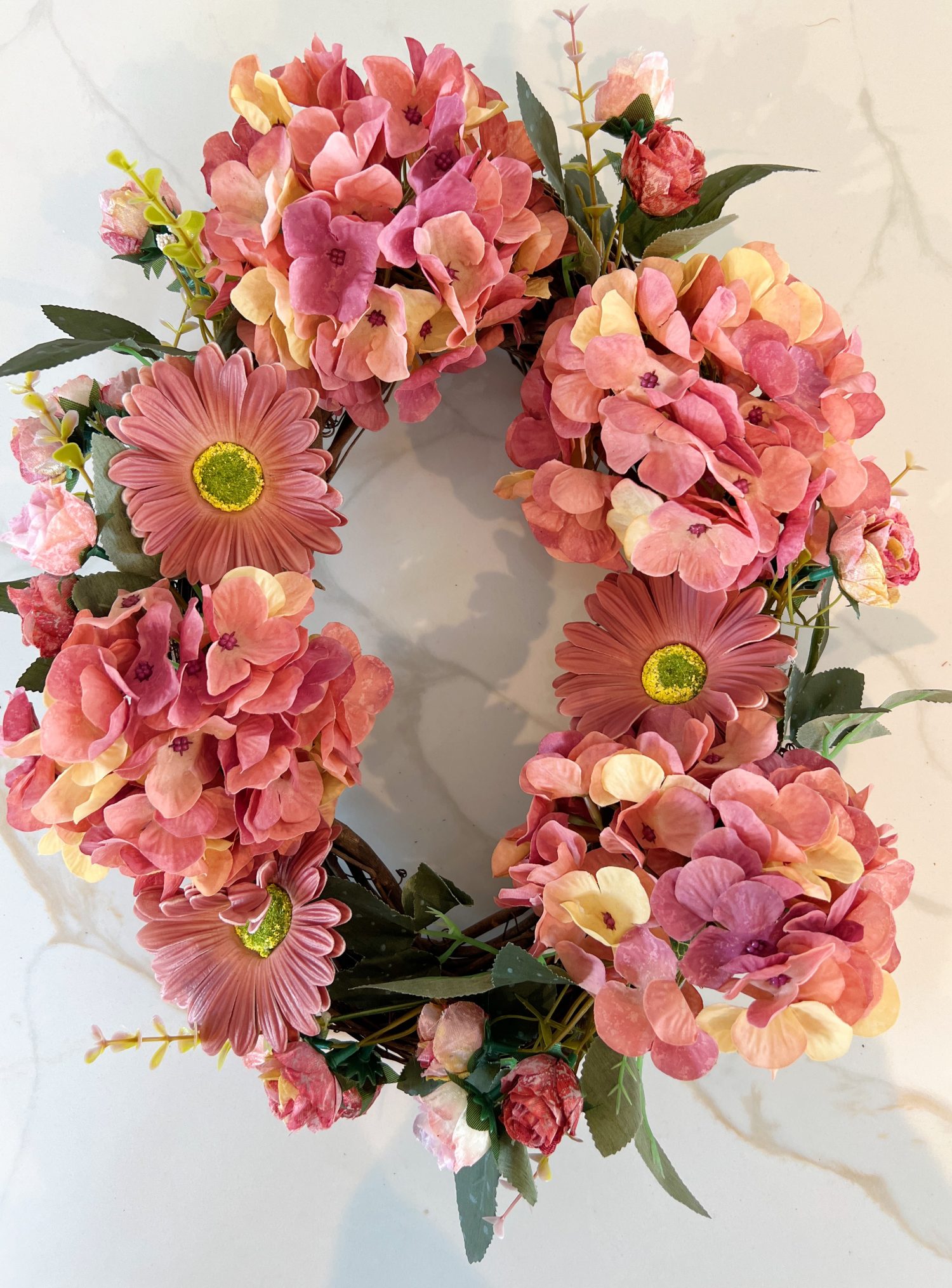 Handmade wreath consisting of faux hydrangeas, gerbera daisies, and roses attached to a grapevine wreath