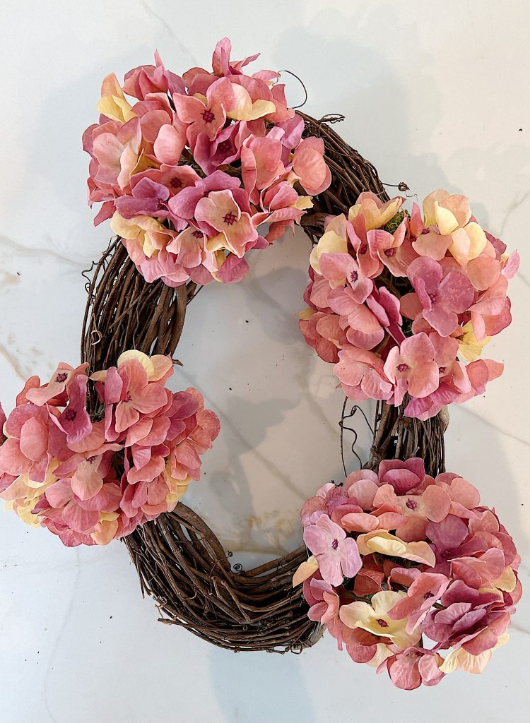 Handmade wreath consisting of faux hydrangeas, gerbera daisies, and roses attached to a grapevine wreath