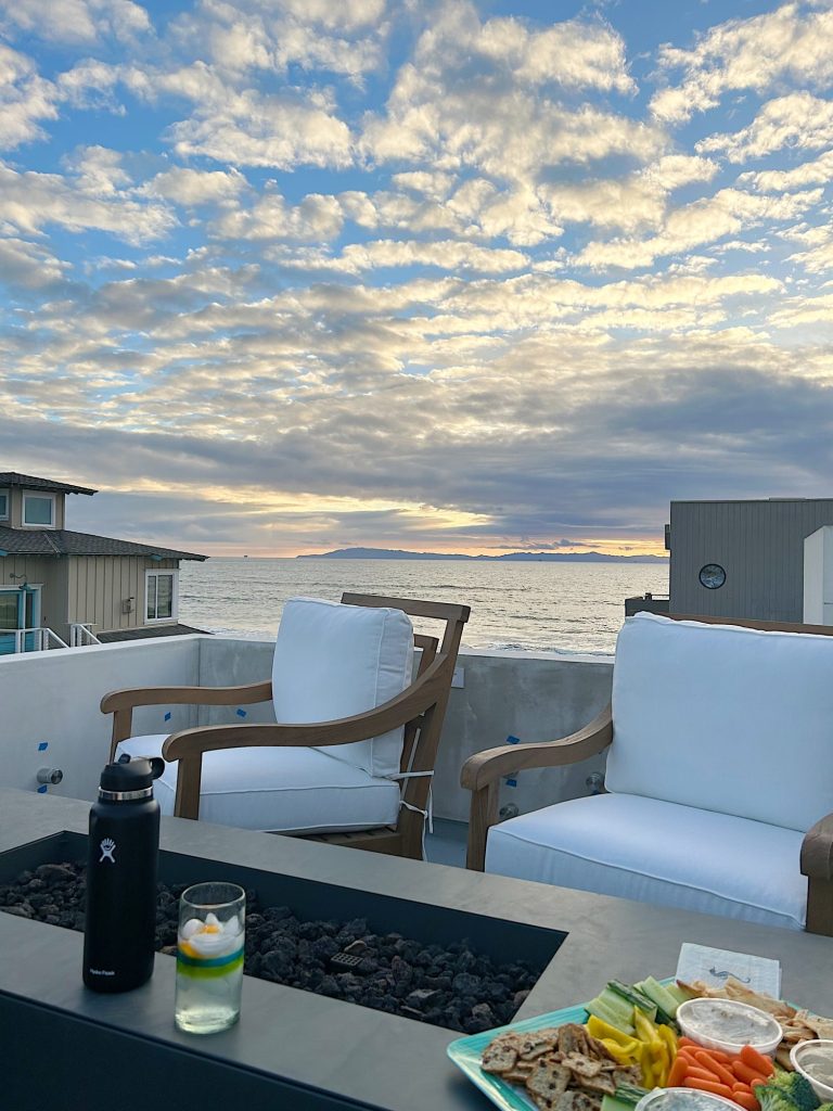 beach deck with two swivel chairs and a fire pit with the sunset in the back ground.