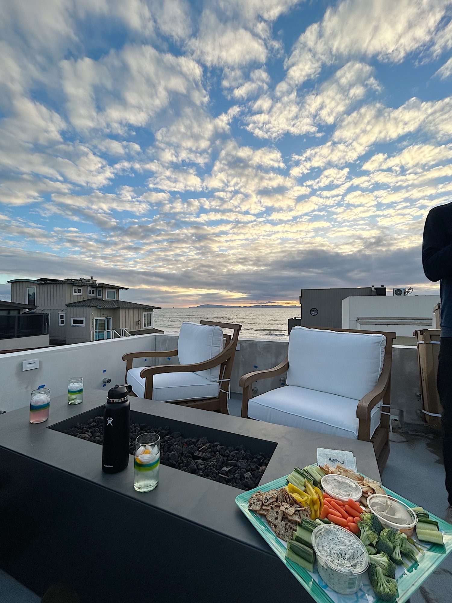 beach deck with two swivel chairs and a fire pit with the sunset in the back ground.