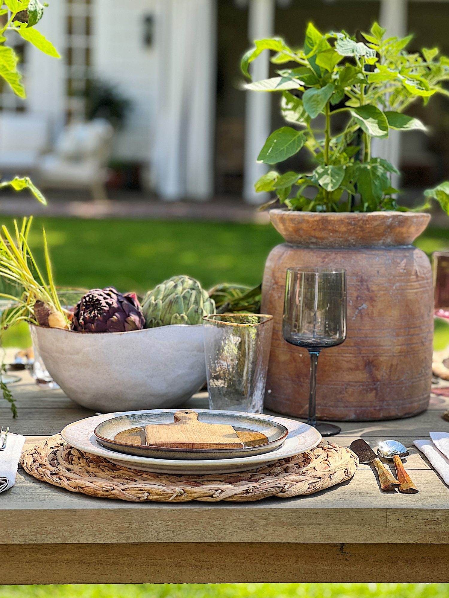 Earth Day dinner with Arhaus table, chairs, plates, colored glassware, salmon salad, copper silverware, and large stoneware vases with live tomato plants.