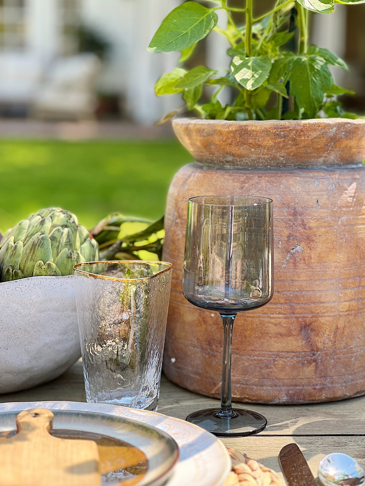 Earth Day dinner with Arhaus table, chairs, plates, colored glassware, salmon salad, copper silverware, and large stoneware vases with live tomato plants.