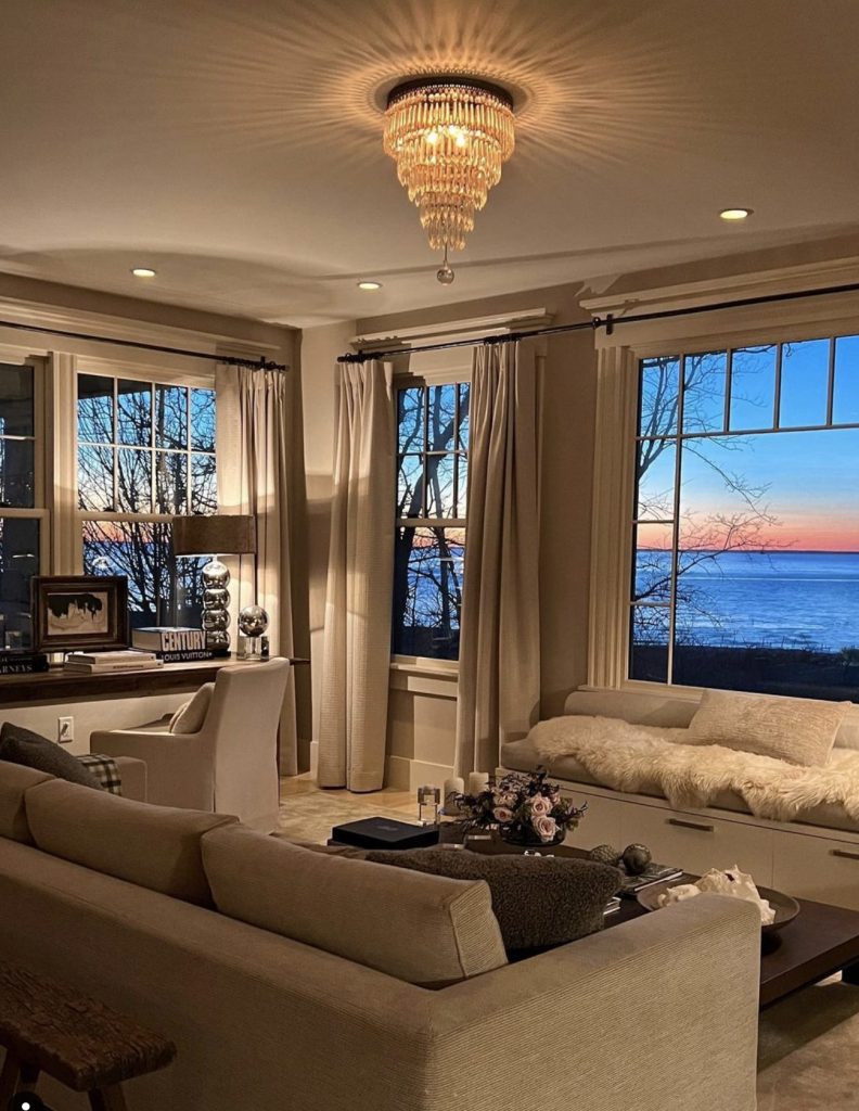 Cozy living room decorated in shades of ivory with expansive windows overlooking water at sunset