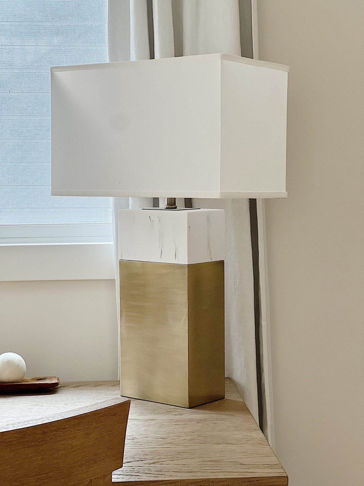 A marble and gold table lamp sitting on a wood desk.