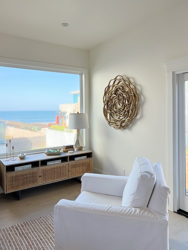 A cane media cabinet with decor and a modern gold lamp and a view of the ocean.